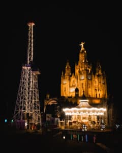Fotografía urbana nocturna, con atracciones de feria en primer plano e iglesia en el fondo.