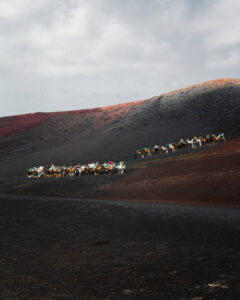 Fotografía de paisaje desértico, montaña arenosa con grupo de camellos y personas