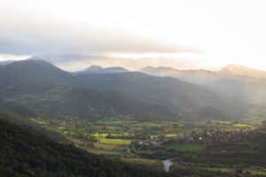 Fotografía de paisaje natural primaveral, con tonos verdes y montañas de fondo con nubes bajas
